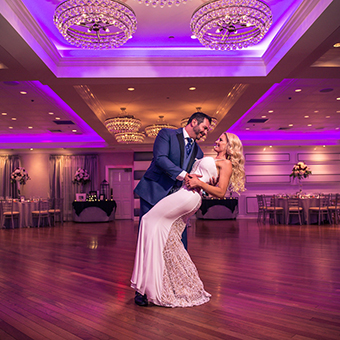 Groom dips bride on the dance floor under purple up lighting.